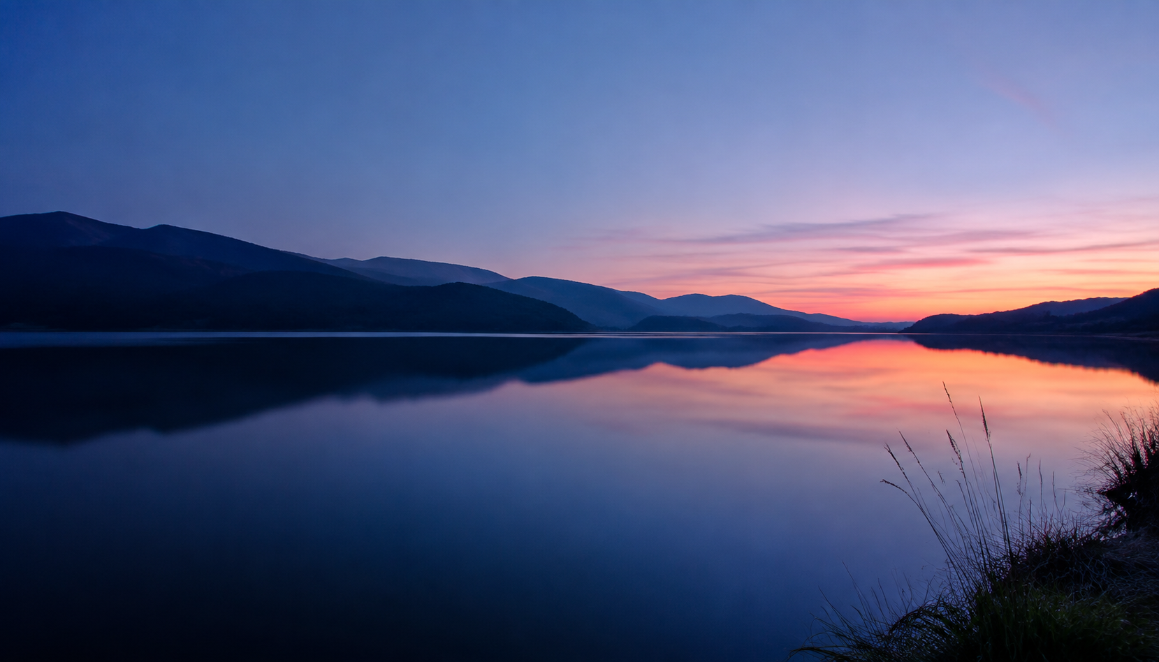 Um lago tranquilo entre montanhas, com a luz suave do entardecer